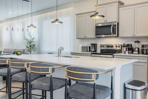A modern kitchen with a central island, bar stools, stainless steel appliances, and pendant lighting.