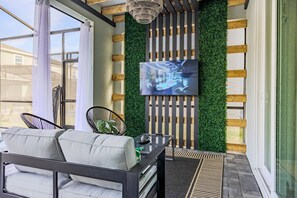 Uma sala de estar moderna com um sofá, uma mesa de centro de vidro, uma TV fixada numa parede verde e um painel ripado de madeira.