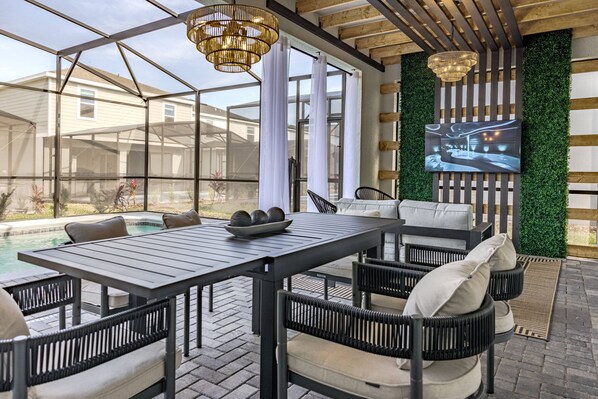 A covered outdoor patio with a pool, seating area, and a television screen.