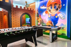 Uma mesa de futebol de mesa, um mural temático do Mario e uma parede de tijolos.