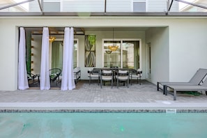 A covered outdoor area with a pool, seating, and a view of the house.
