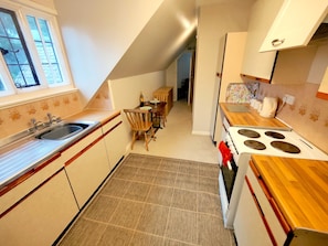 Een keuken met een spoelbak, fornuis en een eettafel met stoelen.
