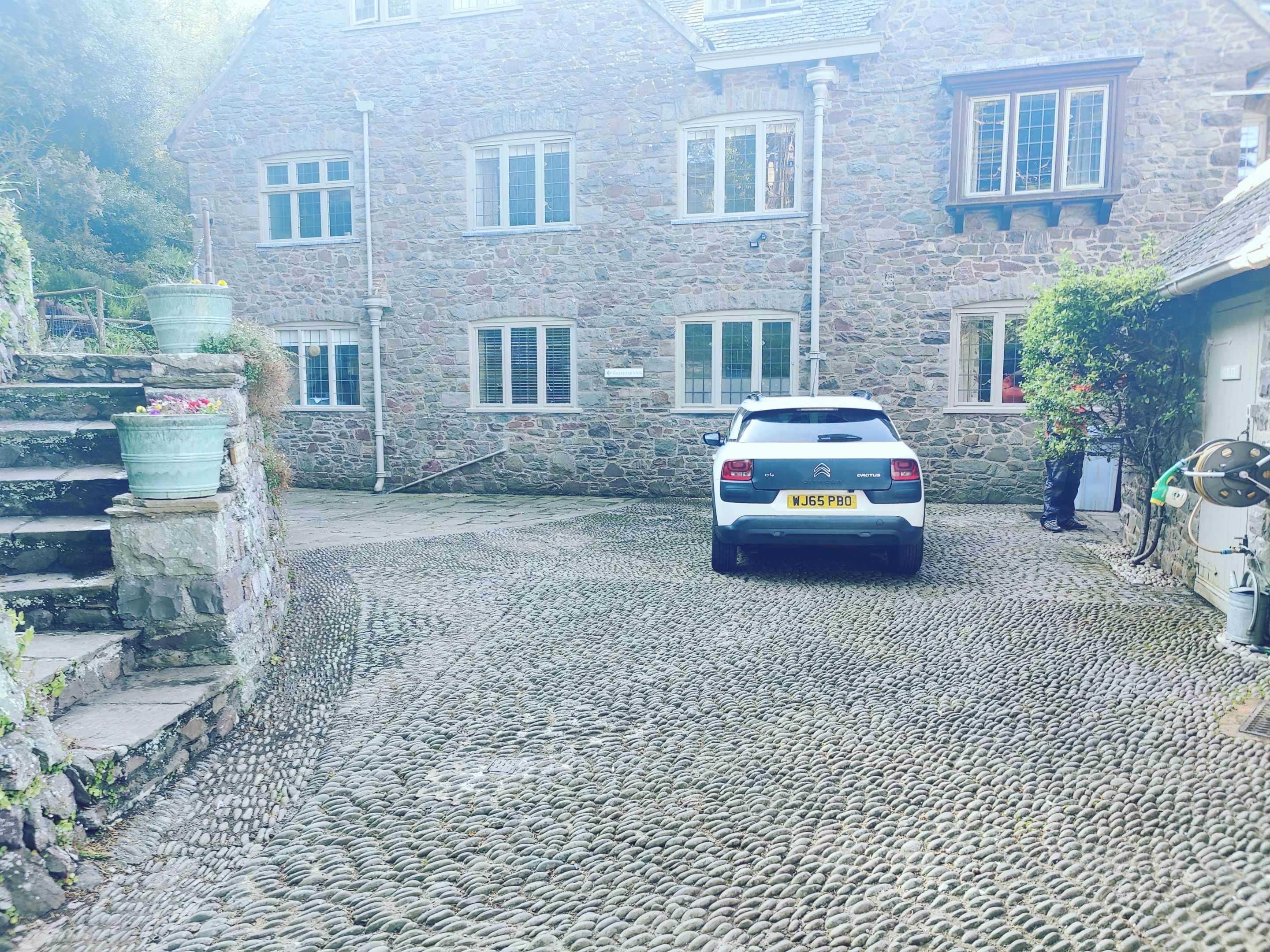 A stone building with a cobblestone driveway and a parked car.