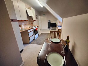 Een eetruimte met een tafel gedekt voor twee personen, een keuken op de achtergrond, en een trap die naar een hoger niveau leidt.