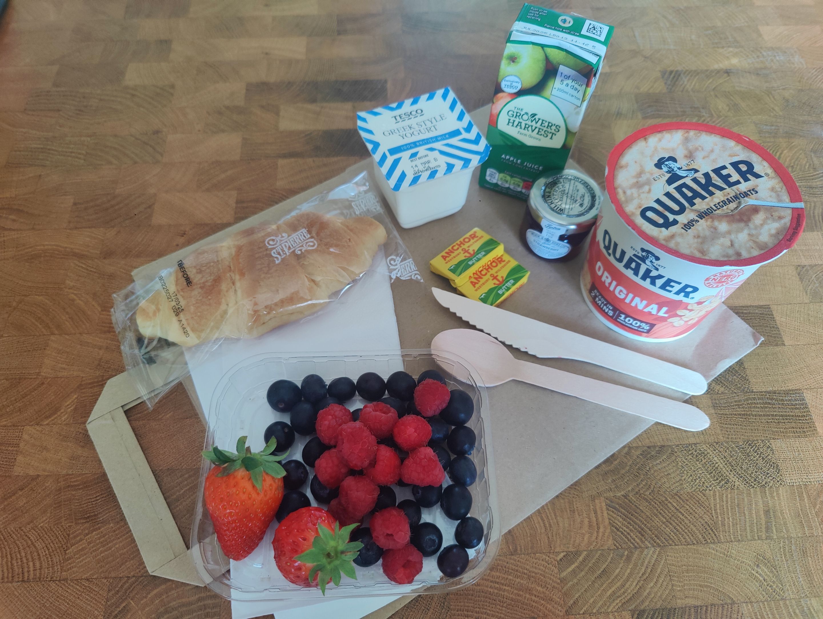 Un pasto con pane, yogurt, frutta e una confezione di avena su un tavolo.