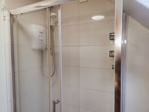 Une douche fermée par des parois en verre, dotée d’un pommeau de douche à main et d’un panneau de commande fixé au mur.