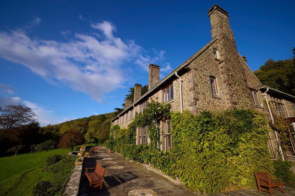 A stone building with a stone chimney, a paved pathway, and wooden chairs.