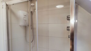 Een douchekabinet met glazen wanden, een handdouche en een bedieningspaneel aan de muur.