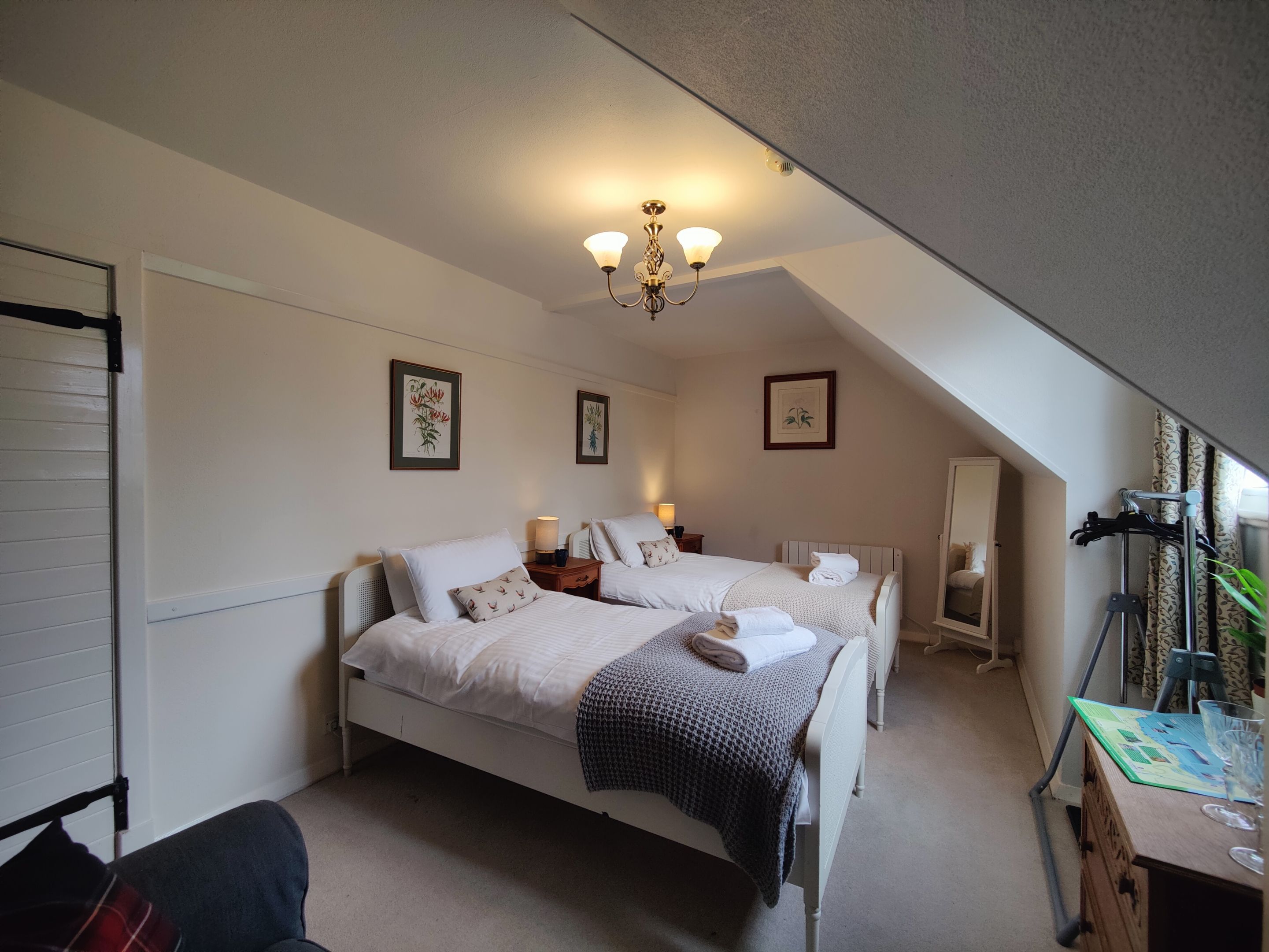 A bedroom with two beds, a chandelier, and a desk with a mirror.