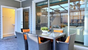 Eine Terrasse mit Glastisch und Korbstühlen, eine Glastür zum Essbereich und eine Deckenleuchte.