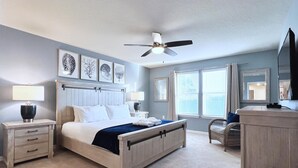 Ein Schlafzimmer mit Bett, Nachttischen, Deckenventilator, Wandkunst und einem Fenster mit Jalousien.