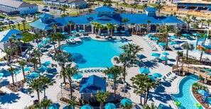 Un resort con piscina central, varias zonas de descanso y palmeras.