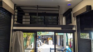 A room with a bunk bed, a desk, and a chair. There is a window with curtains and a view of the outside.