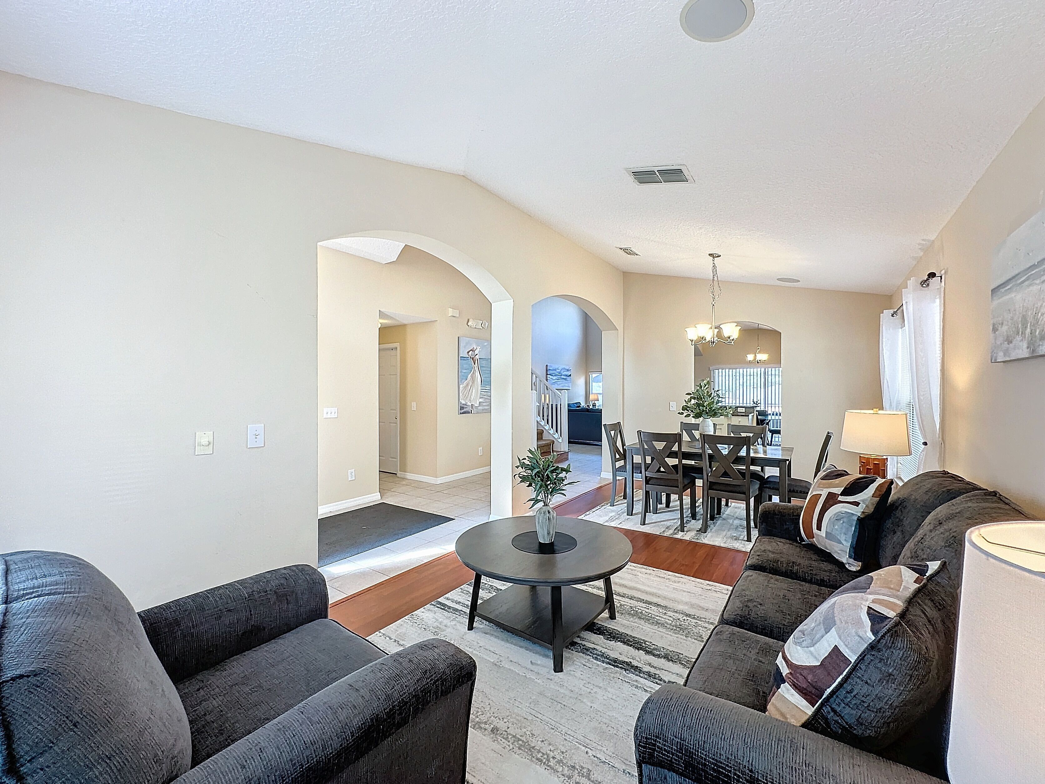 A spacious living room with a sofa set, a coffee table, and a dining area with a chandelier.