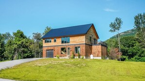 A two-story wooden house with a dark blue roof, a garage, and a small balcony. - Elegant Riverfront house in Rumney with hot tub, outdoors, fitness equipment (Rumney)