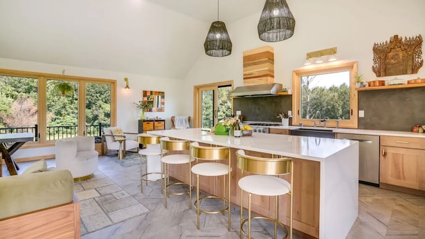 A modern kitchen with a large island, bar stools, pendant lighting, and a view of the outdoors. - Elegant Riverfront house in Rumney with hot tub, outdoors, fitness equipment (Rumney)