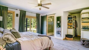 A bedroom with a bed, a ceiling fan, a sliding glass door to a balcony, and a storage unit with shelves. - Elegant Riverfront house in Rumney with hot tub, outdoors, fitness equipment (Rumney)