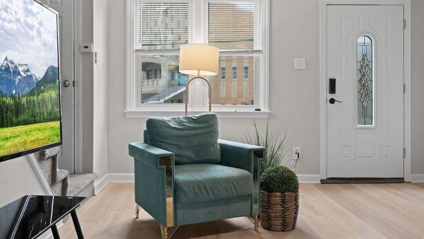 Un salon comprenant un fauteuil de couleur turquoise, une lampe sur pied, un téléviseur et une porte ornée d’un panneau de verre décoratif.