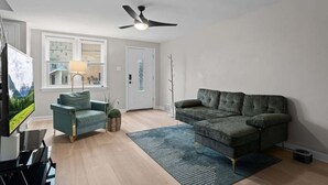Un salon avec un canapé, un fauteuil, un téléviseur et un ventilateur de plafond.