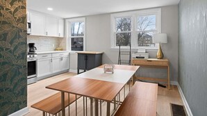 Une cuisine moderne avec des meubles blancs, une table à manger en bois et une fenêtre donnant sur l’extérieur.