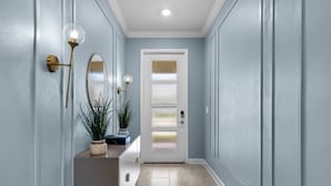 A hallway with light blue walls, a white door with frosted glass panels, and a potted plant on a console table. - Disney! Private Pool, Hot Tub, Game Room & Themed Bedrooms. Book Now! #CG772 (Orlando)