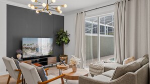 Ein modernes Wohnzimmer mit großem Flachbildfernseher, bequemen Sitzmöglichkeiten, einem Holztisch und einem großen Fenster mit Vorhängen.