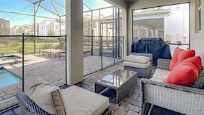 Een ruim terras met glazen omheining, rieten meubilair en een barbecue.
