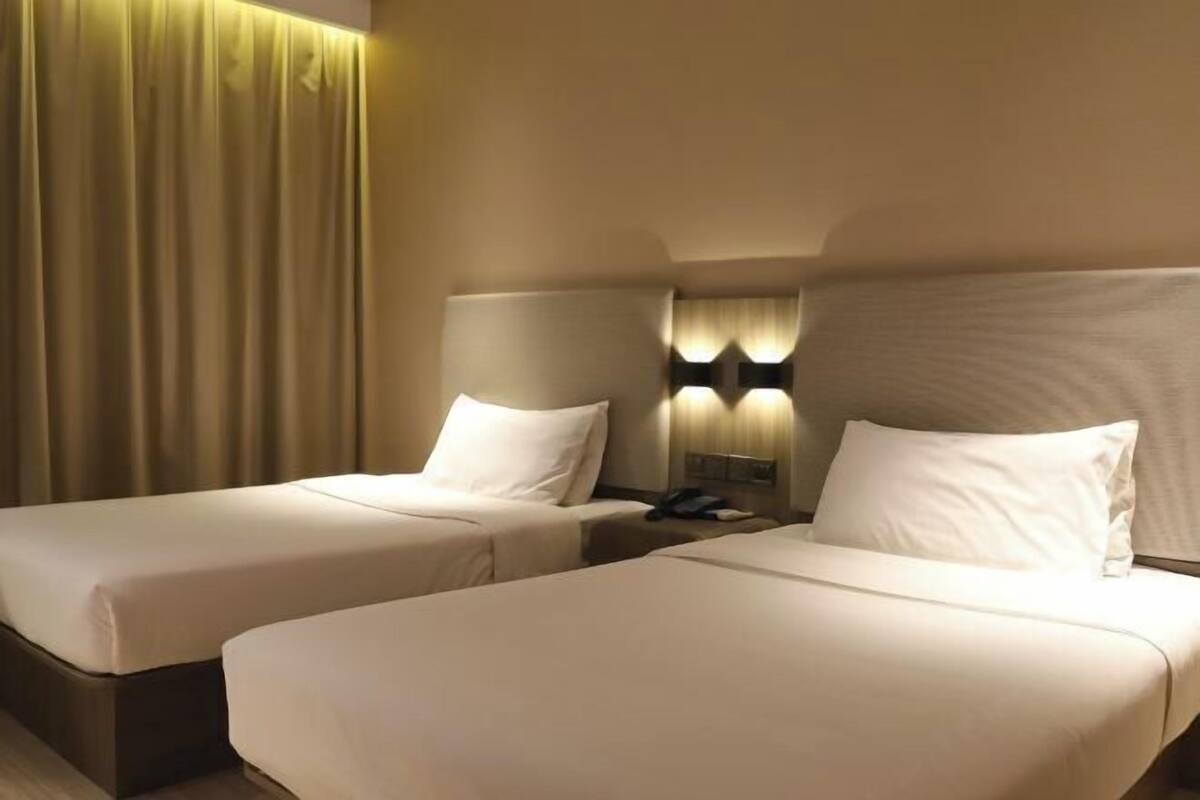 A hotel room with two single beds, a nightstand with a lamp, and a curtain.