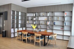 A modern library with a wooden table and chairs, surrounded by bookshelves. - Hanting Hotel (Yanggu Gushan Road) (Yanggu)