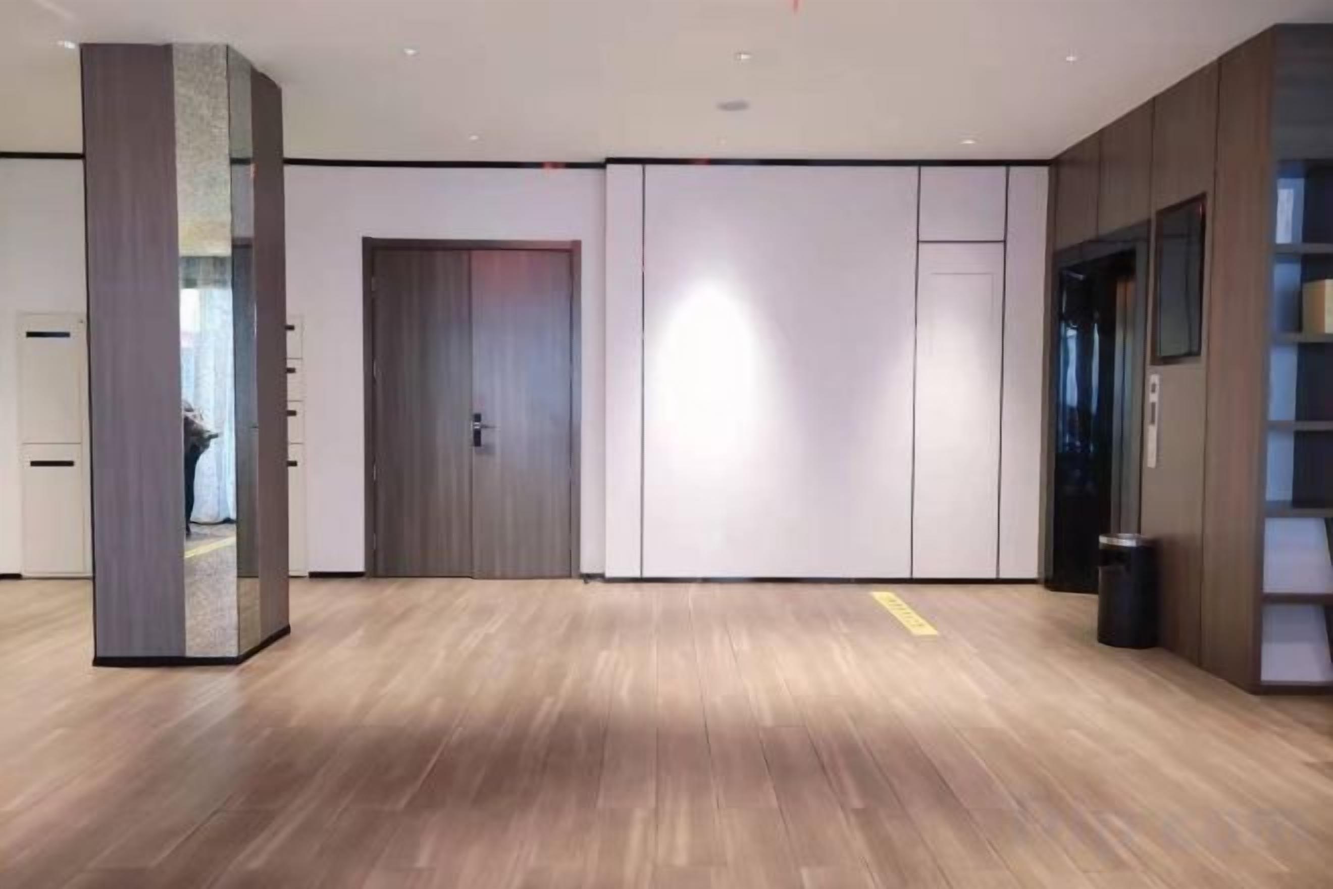 A hotel lobby with a wooden floor, a sliding door, a trash bin, and a bookshelf.