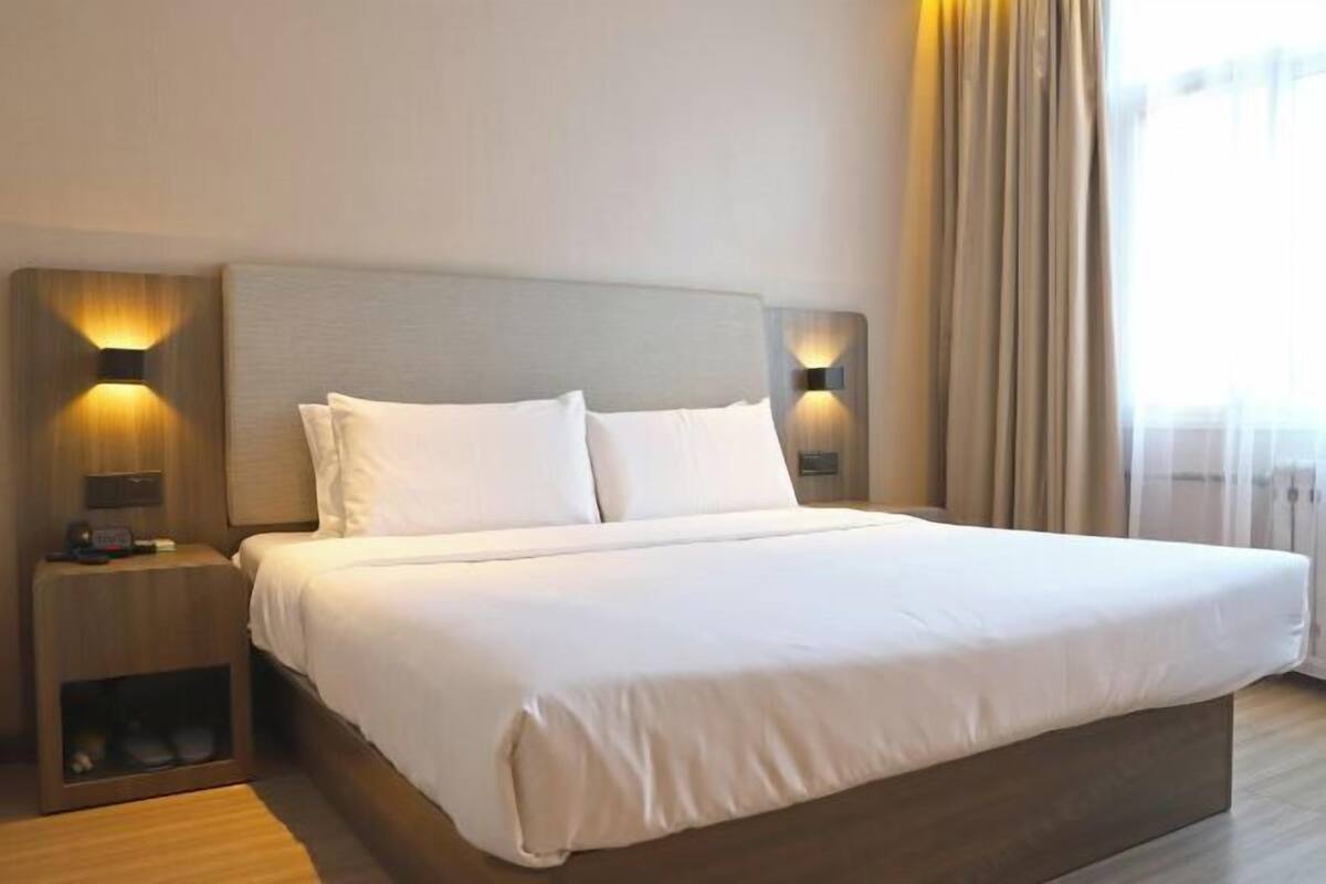 A modern hotel room with a large bed, two bedside tables, and a headboard with integrated lighting.
