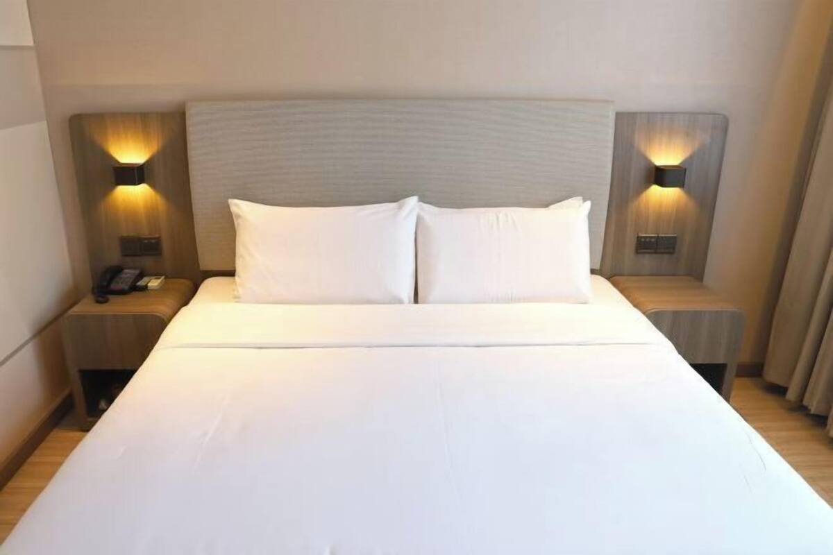 A hotel room with a large bed, two bedside tables, and wall-mounted lamps.