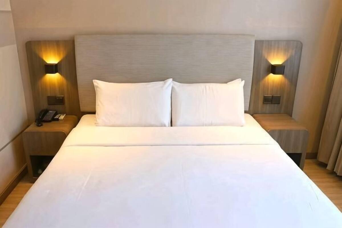 A hotel room with a large bed, two bedside tables, and wall-mounted lamps.