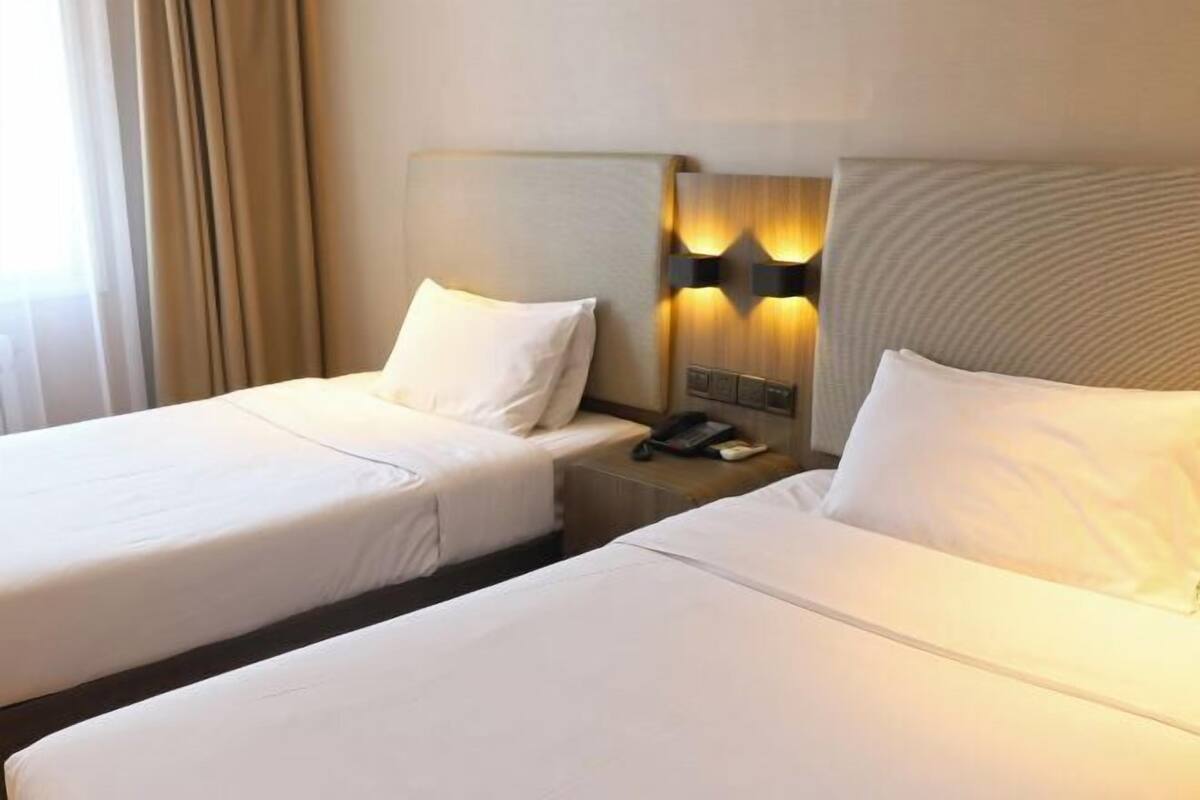A hotel room with two single beds, a bedside table with a phone, and a wall-mounted light fixture.