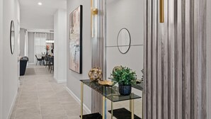 A modern hallway with a glass console table, a potted plant, and a framed artwork on the wall.