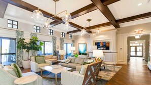 A spacious lobby with a high ceiling, wooden beams, and a large plant. There are multiple seating areas with sofas and chairs, and a television screen is visible in the background.