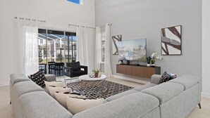 A spacious living room with a grey sofa set, a coffee table, and a TV mounted on the wall. - Disney! Private Pool, Hot Tub, Game Room & Themed Bedrooms. Book Now! #CG777 (Orlando)