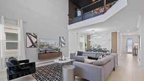 A spacious living room with a grey sofa, black armchair, and a coffee table. A staircase leads to an upper level with a balcony. - Disney! Private Pool, Hot Tub, Game Room & Themed Bedrooms. Book Now! #CG777 (Orlando)