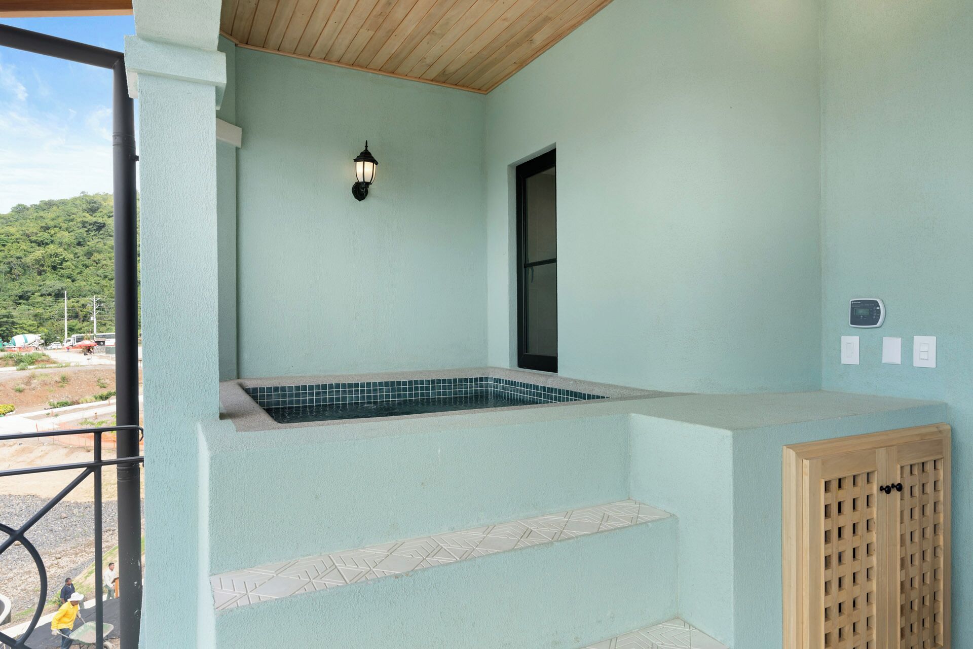 A spa area with a tiled hot tub, a wooden door, and a wall-mounted light fixture.