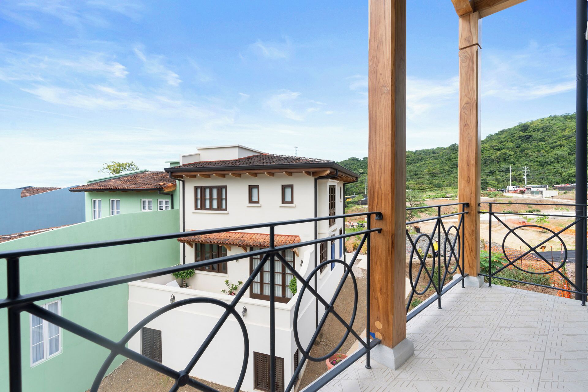 A balcony with a metal railing overlooking a residential area with houses and a view of the sea.