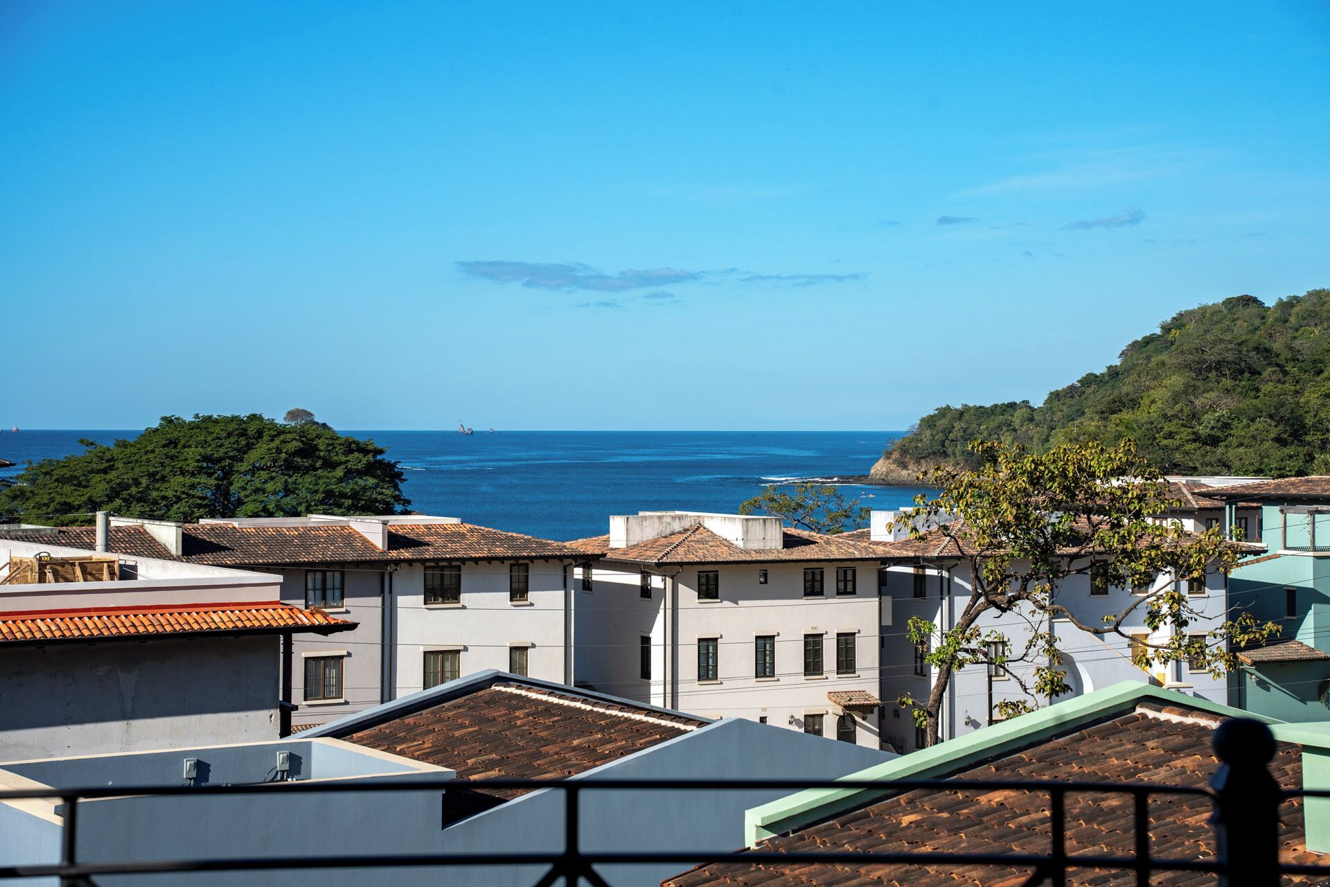 Eine Küstenstadt mit Häusern mit Terrakotta-Dächern, wolkenlosem, blauem Himmel und Blick aufs Meer.