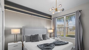 A modern hotel room with a large bed, bedside lamps, a nightstand, and a window with blinds.