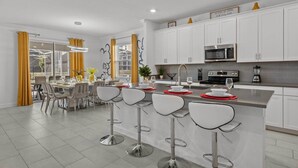 A modern kitchen with white cabinets, a stainless steel microwave, and a bar area with stools. - Disney! Private Pool, Hot Tub, Game Room & Themed Bedrooms. Book Now! #CG788 (Orlando)