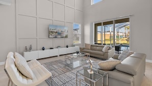 A spacious living room with a large window, a sofa, a coffee table, and a TV mounted on the wall. - Disney Getaway! Private Pool & Themed Bedrooms. Book Now! #CG791 (Orlando)