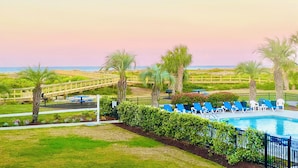 A pool area with blue lounge chairs and a wooden bridge leading to the beach.