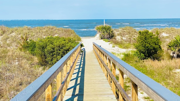 A wooden boardwalk leading to the beach with dunes and vegetation on either side.