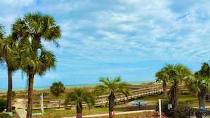 A beach view with palm trees, a wooden boardwalk, and a picnic table.