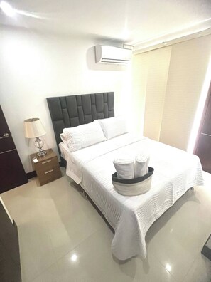 A hotel room with a bed, a nightstand, a lamp, and an air conditioning unit. - Edificio Fence Real (Cali)