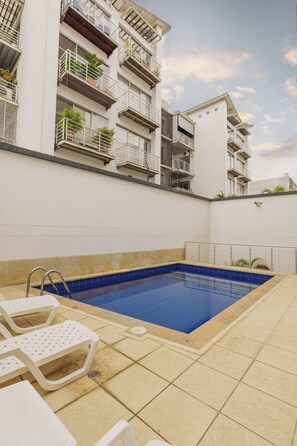 A rooftop swimming pool with a blue interior, surrounded by white lounge chairs and a white building with balconies. - Edificio Fence Real (Cali)