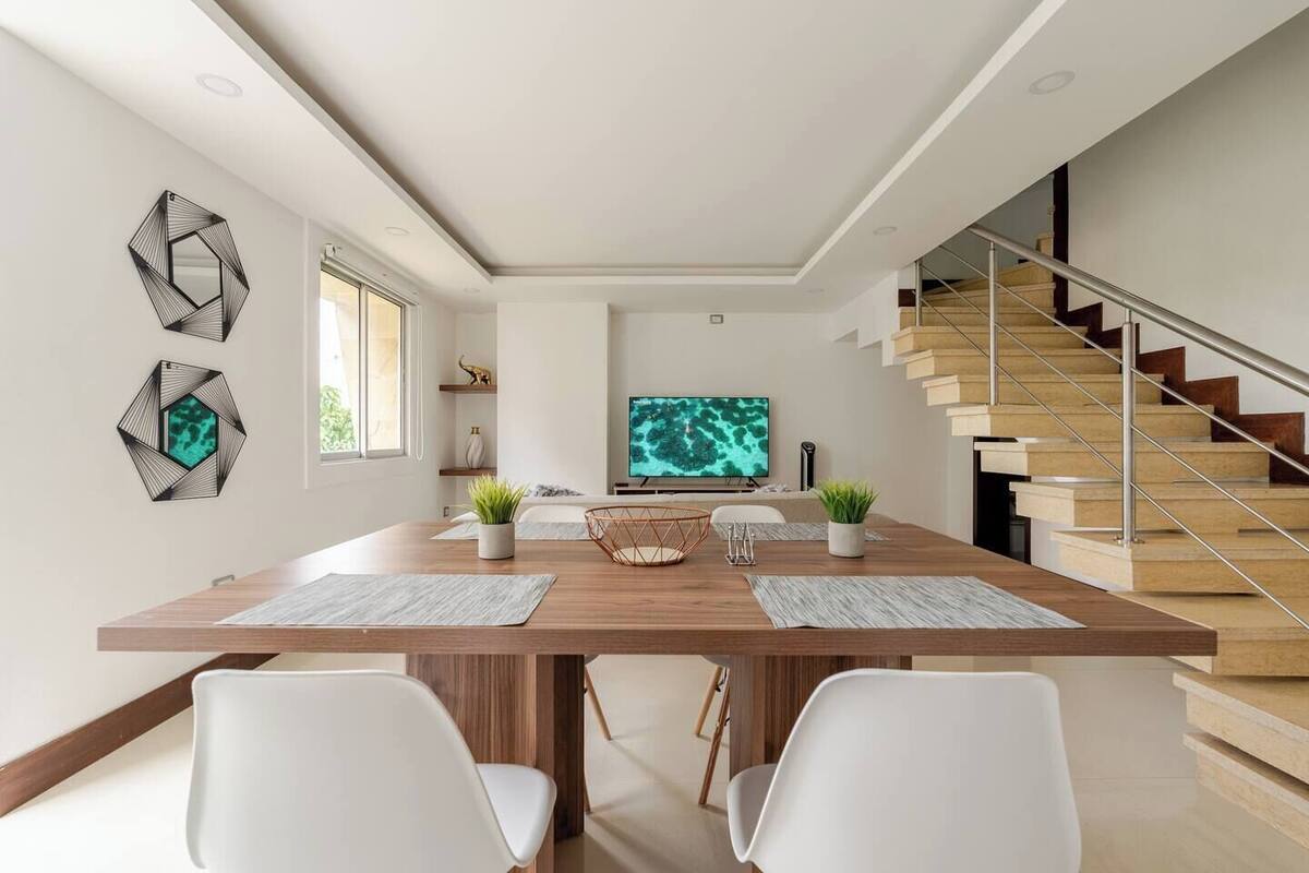Ein moderner Essbereich mit Holztisch, weißen Stühlen und einem großen Flachbildfernseher.